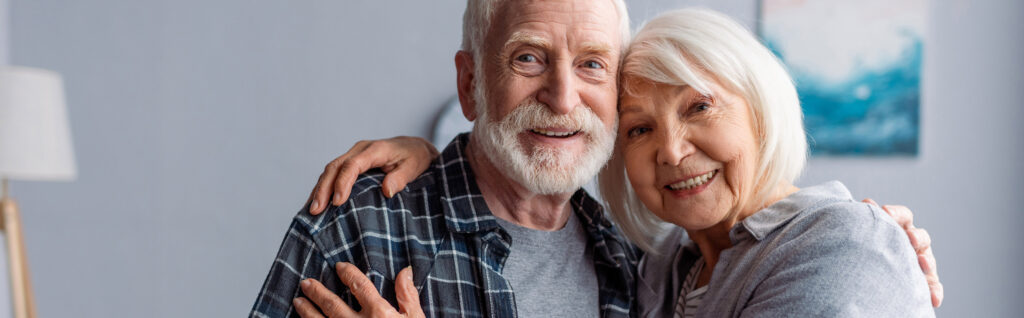 Horizontal image of happy senior couple smiling and embracing while looking at camera.